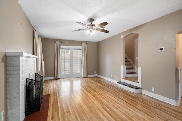 506 6th Ave SW, Austin, MN 55912 - unfurnished living room with a ceiling fan, arched walkways, a brick fireplace, stairway, and light wood-style floors