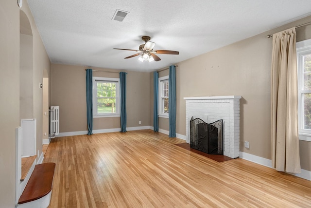506 6th Ave SW, Austin, MN 55912 - unfurnished living room with radiator heating unit, light wood-type flooring, a fireplace, and ceiling fan