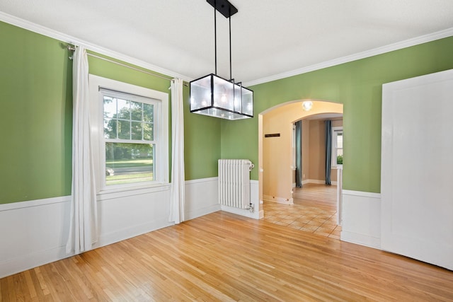 506 6th Ave SW, Austin, MN 55912 - unfurnished room featuring radiator, arched walkways, light wood-style floors, crown molding, and wainscoting