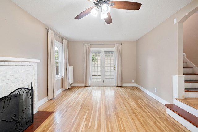 506 6th Ave SW, Austin, MN 55912 - unfurnished living room featuring stairway, light wood-type flooring, a ceiling fan, a brick fireplace, and arched walkways