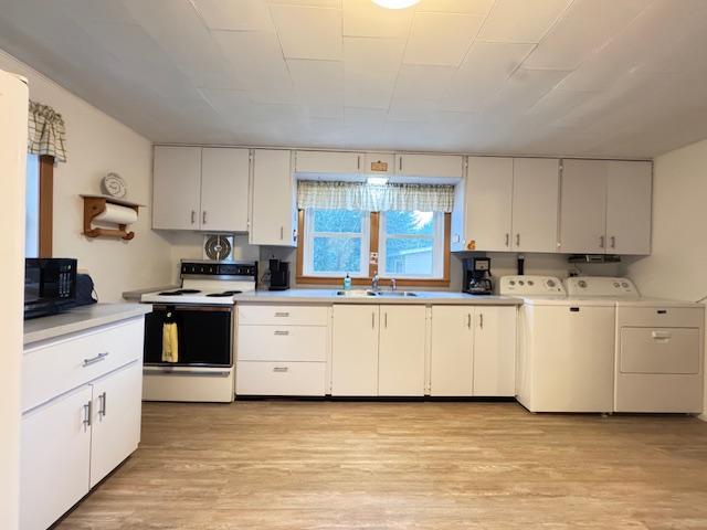 317 2nd St NE, Menahga, MN 56464 - kitchen with washer and dryer, white range with electric stovetop, light wood-style flooring, light countertops, and white cabinets