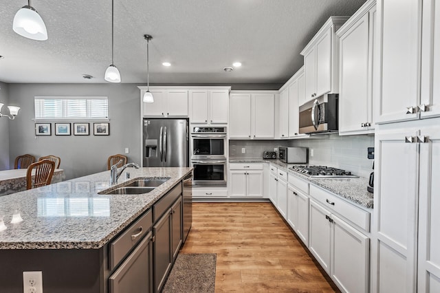 4870 Copper Ridge Dr, Woodbury, MN 55129 - kitchen featuring appliances with stainless steel finishes, white cabinets, light wood-style floors, decorative light fixtures, and a textured ceiling