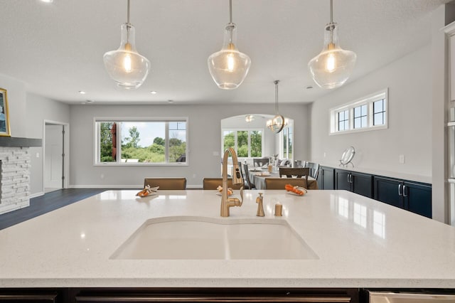 19400 75th Ave, Corcoran, MN 55340 - kitchen featuring open floor plan, light stone counters, hanging light fixtures, a chandelier, and a stone fireplace