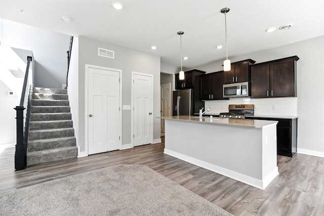 6450 Inspire Cir S, Cottage Grove, MN 55016 - kitchen featuring appliances with stainless steel finishes, light wood-type flooring, backsplash, light countertops, and a center island with sink