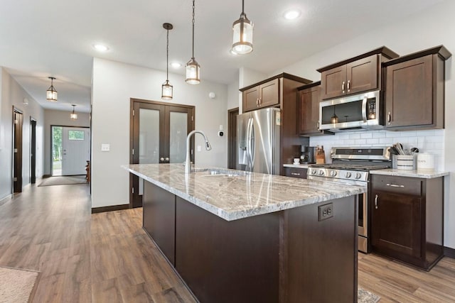 2065 Pleasant Dr, Prescott, WI 54021 - kitchen featuring stainless steel appliances, dark brown cabinetry, decorative backsplash, a center island with sink, and light wood-type flooring