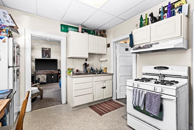 702 11th St, Duluth, MN 55805 - kitchen with white gas range, under cabinet range hood, a paneled ceiling, white cabinets, and decorative backsplash