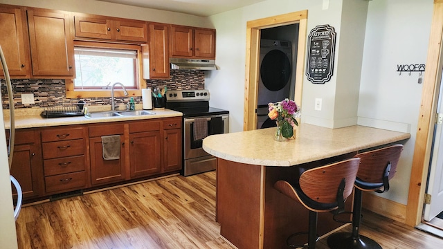 315 Woodworth St, Elmwood, WI 54740 - kitchen featuring stainless steel electric range, under cabinet range hood, stacked washing machine and dryer, light wood-type flooring, and brown cabinetry