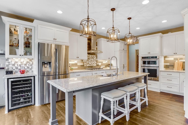 2064 141st Ln NE, Ham Lake, MN 55304 - kitchen featuring stainless steel appliances, beverage cooler, wall chimney range hood, tasteful backsplash, and white cabinets