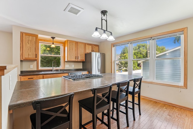 1661 Bush Ave, Saint Paul, MN 55106 - kitchen with appliances with stainless steel finishes, dark countertops, a kitchen breakfast bar, pendant lighting, and light wood-style floors