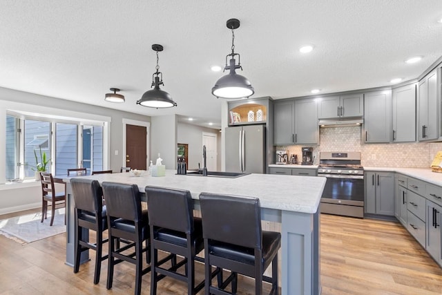 905 Sellards Dr, Dassel, MN 55325 - kitchen featuring stainless steel appliances, gray cabinetry, under cabinet range hood, light countertops, and light wood-style flooring