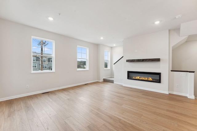 7415 E Ramsey Pkwy NW, Ramsey, MN 55303 - unfurnished living room with light wood-type flooring, recessed lighting, a glass covered fireplace, and stairs