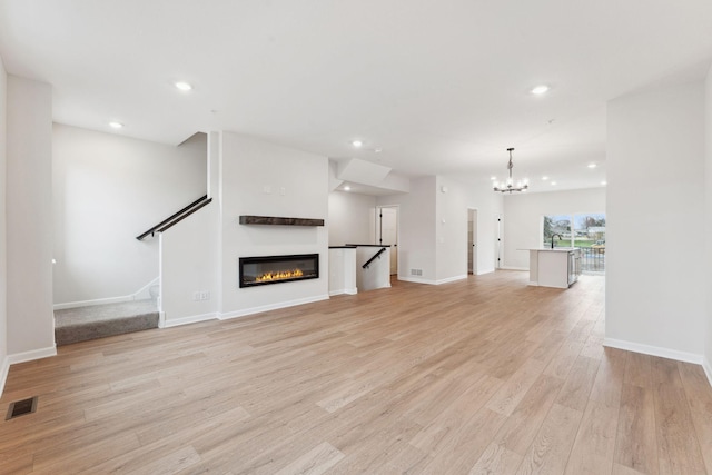 7415 E Ramsey Pkwy NW, Ramsey, MN 55303 - unfurnished living room with a chandelier, light wood-style floors, recessed lighting, a glass covered fireplace, and stairs