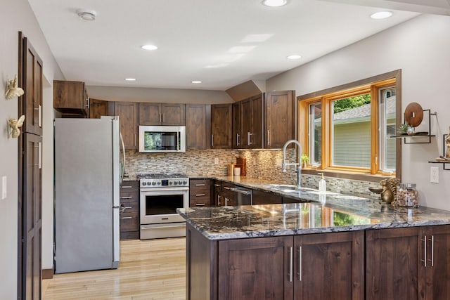 708 Riverside Dr N, North Hudson, WI 54016 - kitchen with appliances with stainless steel finishes, light wood-style floors, dark stone counters, dark brown cabinetry, and a peninsula