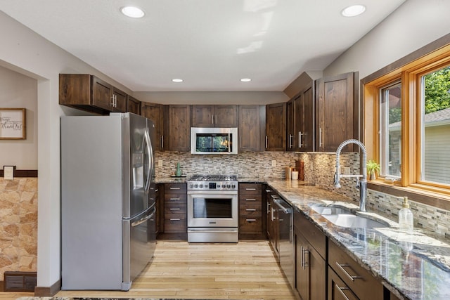 708 Riverside Dr N, North Hudson, WI 54016 - kitchen with stainless steel appliances, light stone counters, light wood-type flooring, dark brown cabinetry, and backsplash