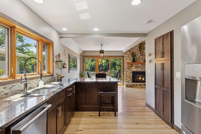 708 Riverside Dr N, North Hudson, WI 54016 - kitchen with stainless steel appliances, light wood-style flooring, stone counters, a peninsula, and a stone fireplace