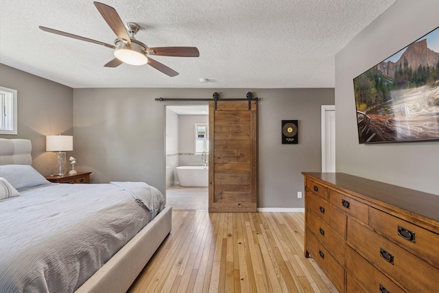 708 Riverside Dr N, North Hudson, WI 54016 - bedroom featuring a barn door, a textured ceiling, light wood-type flooring, connected bathroom, and ceiling fan