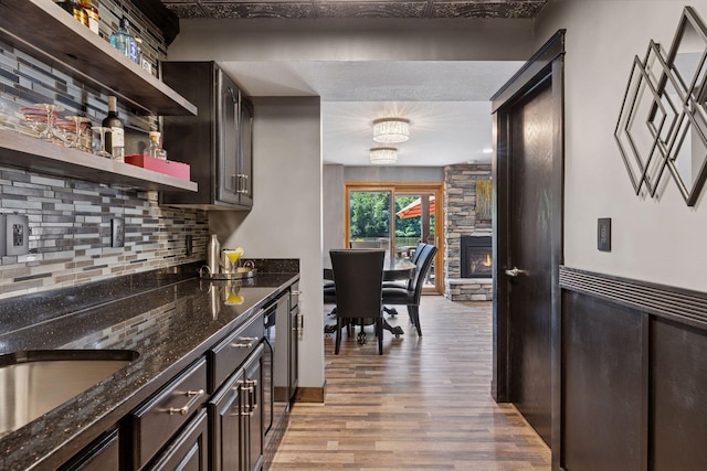 708 Riverside Dr N, North Hudson, WI 54016 - kitchen featuring light wood-style floors, open shelves, backsplash, dark stone countertops, and a stone fireplace