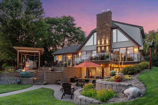 708 Riverside Dr N, North Hudson, WI 54016 - back of house at dusk featuring a patio area, a chimney, a lawn, and a balcony