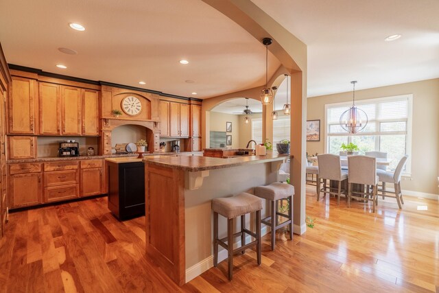 60515 235th St, Madison Lake, MN 56063 - kitchen featuring a breakfast bar area, a peninsula, wood finished floors, brown cabinetry, and arched walkways