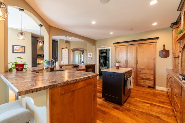 60515 235th St, Madison Lake, MN 56063 - kitchen featuring wood finished floors, a kitchen island, arched walkways, recessed lighting, and brown cabinets