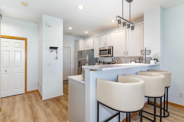 14399 Banyan Ln, Rosemount, MN 55068 - kitchen featuring appliances with stainless steel finishes, a breakfast bar, tasteful backsplash, a peninsula, and light wood-style floors