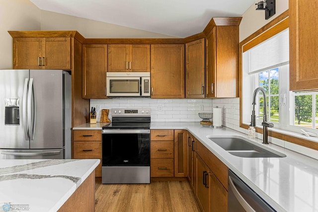 4515 Westport Pkwy, Fargo, ND 58078 - kitchen featuring appliances with stainless steel finishes, vaulted ceiling, brown cabinets, light wood-type flooring, and backsplash
