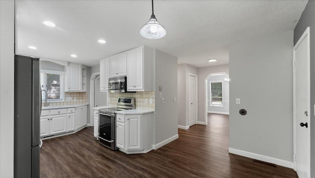 12720 Ibis St NW, Coon Rapids, MN 55448 - kitchen with appliances with stainless steel finishes, arched walkways, dark wood-style flooring, tasteful backsplash, and white cabinetry