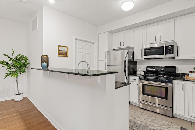 2566 Ellis Ave Unit 103, Saint Paul, MN 55114 - kitchen featuring stainless steel appliances, dark stone counters, a peninsula, white cabinets, and light wood-type flooring
