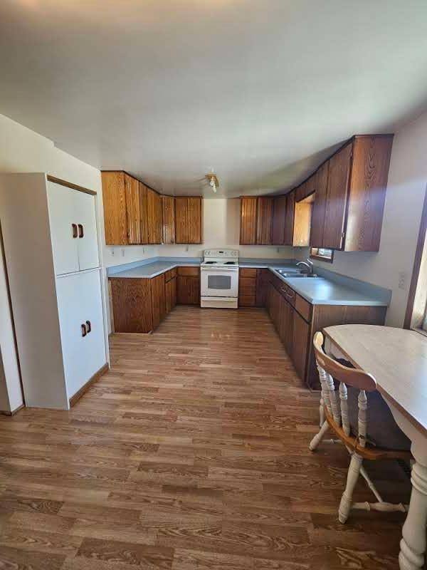 15596 464th St, Hewitt, MN 56453 - kitchen featuring white electric stove, wood finished floors, brown cabinetry, and light countertops
