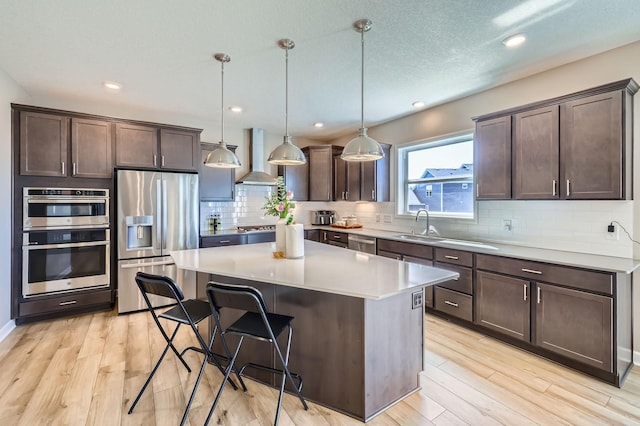 11887 73rd St NE, Otsego, MN 55301 - kitchen featuring appliances with stainless steel finishes, wall chimney exhaust hood, dark brown cabinetry, light wood-style flooring, and tasteful backsplash