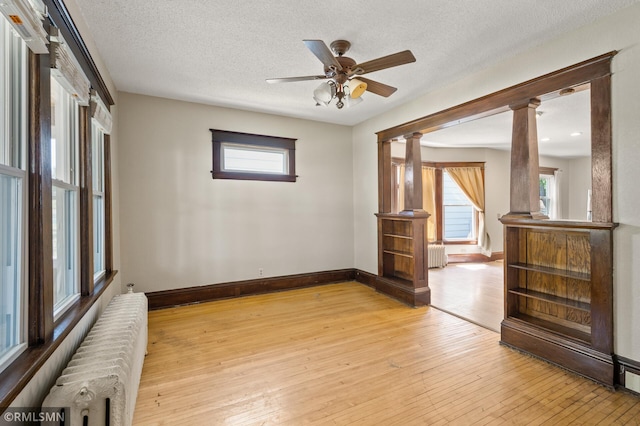 727 Virginia St, Saint Paul, MN 55103 - empty room featuring radiator heating unit, ornate columns, light wood-type flooring, plenty of natural light, and a textured ceiling