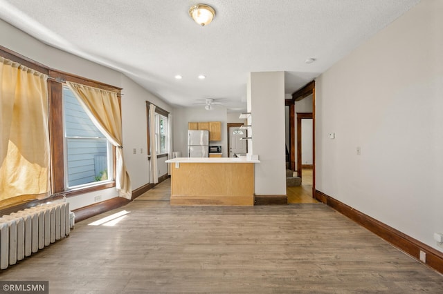 727 Virginia St, Saint Paul, MN 55103 - kitchen with radiator heating unit, freestanding refrigerator, light countertops, light wood-style flooring, and a peninsula