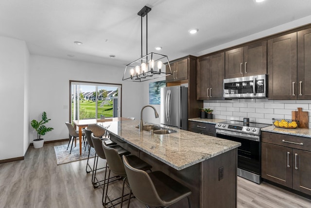 12910 Brenly Way, Rogers, MN 55374 - kitchen with appliances with stainless steel finishes, light stone counters, backsplash, a center island with sink, and dark brown cabinetry