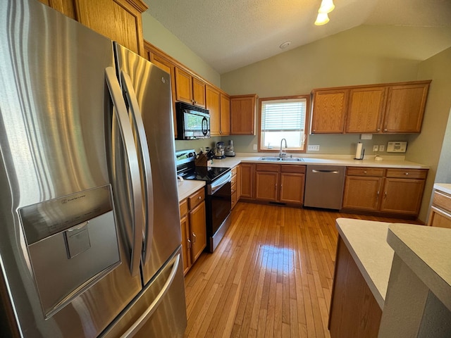 1070 20th St NE, Owatonna, MN 55060 - kitchen featuring stainless steel appliances, brown cabinets, light wood-type flooring, lofted ceiling, and light countertops