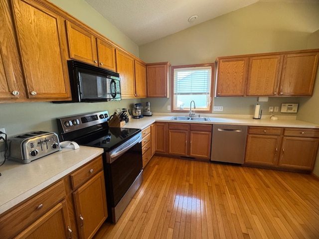 1070 20th St NE, Owatonna, MN 55060 - kitchen with stainless steel appliances, brown cabinetry, vaulted ceiling, light countertops, and light wood-type flooring