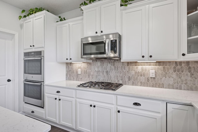12745 39th St NE, Saint Michael, MN 55376 - kitchen with appliances with stainless steel finishes, white cabinets, decorative backsplash, glass insert cabinets, and light stone countertops