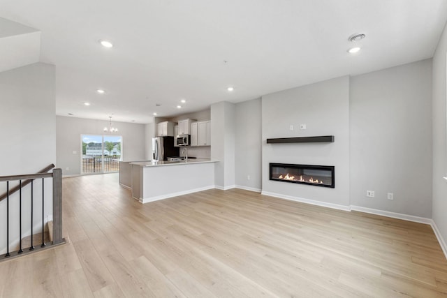 7407 E Ramsey Pkwy NW, Ramsey, MN 55303 - unfurnished living room featuring light wood finished floors, a glass covered fireplace, recessed lighting, and a chandelier