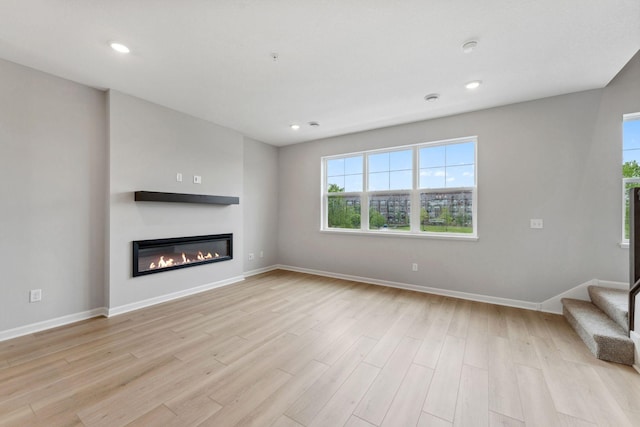 7407 E Ramsey Pkwy NW, Ramsey, MN 55303 - unfurnished living room featuring a glass covered fireplace, light wood-style flooring, stairs, and recessed lighting