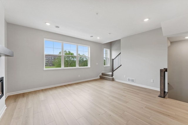 7407 E Ramsey Pkwy NW, Ramsey, MN 55303 - unfurnished living room featuring stairway, light wood-type flooring, recessed lighting, and a glass covered fireplace