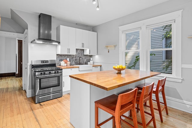 1066 Woodbridge St, Saint Paul, MN 55117 - kitchen featuring wall chimney range hood, stainless steel gas range, butcher block countertops, a breakfast bar, and backsplash