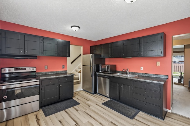 2365 Dorland Ln E, Maplewood, MN 55119 - kitchen featuring appliances with stainless steel finishes, dark countertops, light wood-type flooring, under cabinet range hood, and a textured ceiling