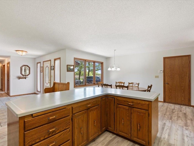 15170 141st Ave, Wadena, MN 56482 - kitchen featuring a textured ceiling, light wood-style floors, brown cabinetry, light countertops, and a chandelier
