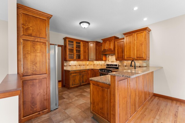 2309 Teakwood Ln SW, Rochester, MN 55902 - kitchen with stainless steel appliances, a peninsula, decorative backsplash, light stone countertops, and brown cabinetry