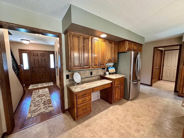 1201 Morningside Cir, Marshall, MN 56258 - kitchen with freestanding refrigerator, built in study area, brown cabinets, a textured ceiling, and tasteful backsplash