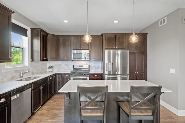 7850 242nd St, Wyoming, MN 55025 - kitchen featuring stainless steel appliances, dark brown cabinetry, tasteful backsplash, light wood-type flooring, and a kitchen bar
