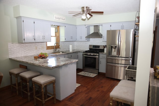 3930 99th Ave NE, Blaine, MN 55014 - kitchen with stainless steel appliances, wall chimney exhaust hood, a peninsula, backsplash, and dark wood-type flooring