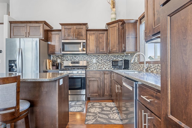 4822 34th Ave S, Fargo, ND 58104 - kitchen featuring stainless steel appliances, stone counters, tasteful backsplash, wood finished floors, and a kitchen bar