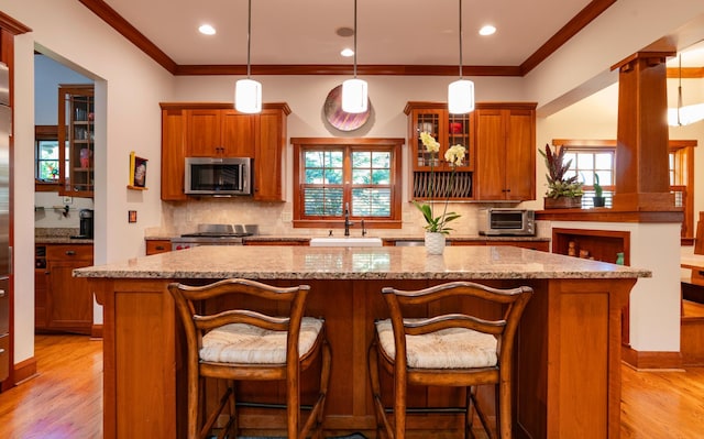 582 Summit Ave, Saint Paul, MN 55102 - kitchen with stainless steel microwave, a center island, light wood-type flooring, brown cabinetry, and tasteful backsplash