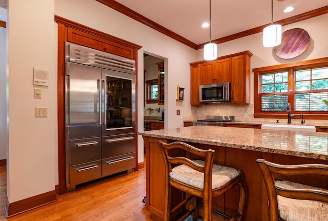 582 Summit Ave, Saint Paul, MN 55102 - kitchen featuring stainless steel appliances, light wood-type flooring, decorative backsplash, brown cabinetry, and light stone countertops