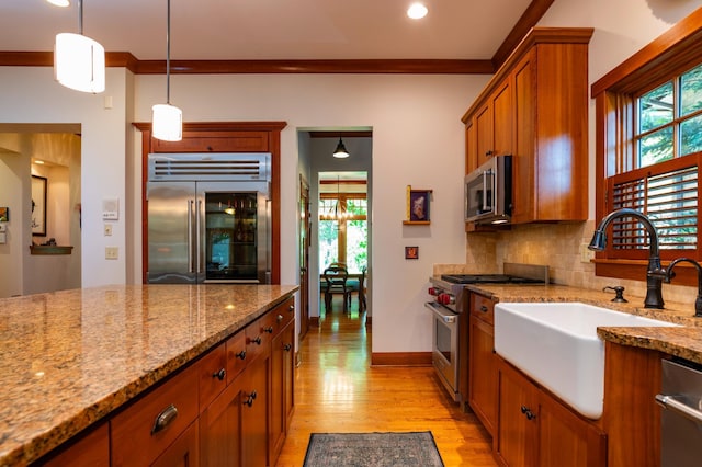 582 Summit Ave, Saint Paul, MN 55102 - kitchen with high quality appliances, brown cabinetry, light wood-style flooring, decorative backsplash, and light stone countertops